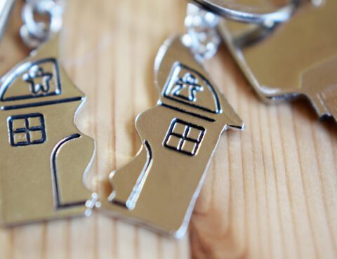 A keychain depicting a house is broken in half, with a key attached to each section.