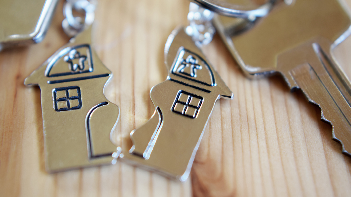 A keychain depicting a house is broken in half, with a key attached to each section.