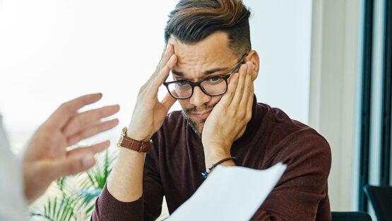 Stressed man holding his head while reviewing paperwork during a financial discussion