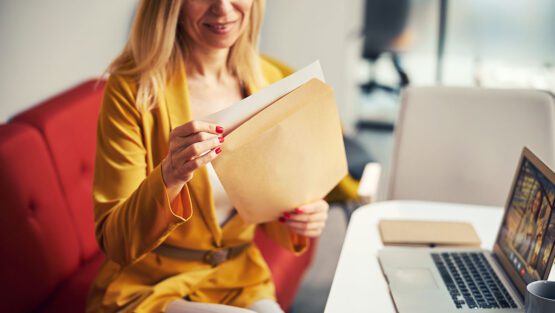 Woman opening a financial envelope while seated at a desk with a laptop