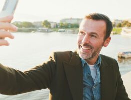 Middle-aged man smiling and taking a selfie near the water, enjoying a moment of happiness and peace after divorce.