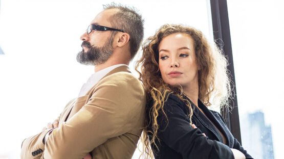 Two professionals standing back to back with arms crossed in a modern office setting