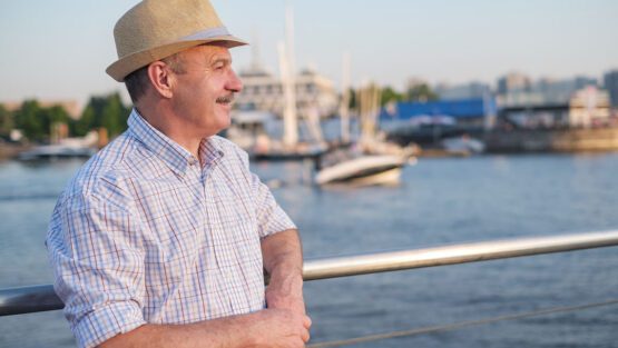 Man standing by a waterfront railing, looking out over boats at a marina during daylight