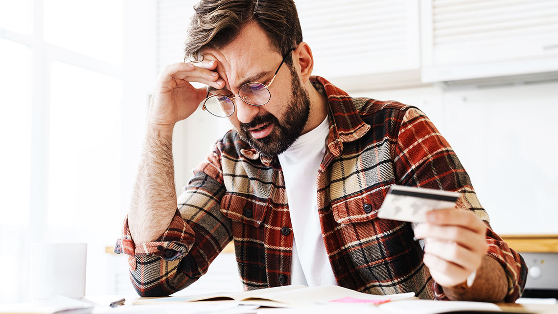 Man reviewing bills and holding a credit card while stressed about divorce finances and financial decisions