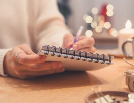 Person writing in a planner beside holiday decorations, representing planning ahead for the holidays during divorce.