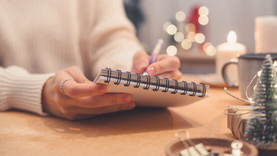 Person writing in a planner beside holiday decorations, representing planning ahead for the holidays during divorce.